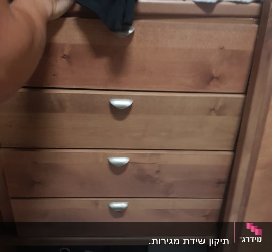 יד פותחת מגירת עץ בארון בגדים